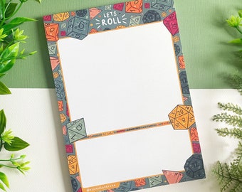 May include: A notepad with a white background and a border of colorful dice. The border has the text "LETS ROLL" in a yellow banner. The notepad is on a green and white surface.