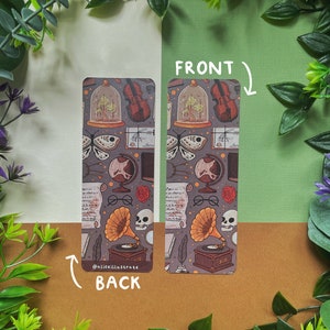 May include: A double-sided bookmark with a vintage aesthetic. The front features a repeating pattern of a violin, a globe, a skull, a magnifying glass, a rose, a book, a feather, and a glass dome with a tree inside. The back features the same pattern with the addition of a gramophone and the text "@aliceillustrate".