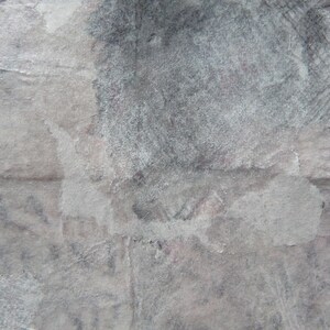 May include: A close-up of a textured, gray surface with a white, faded, and slightly textured area. The surface appears to be made of paper or cardboard.