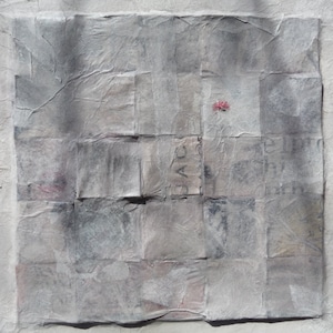 May include: A gray and white abstract art piece made of layered paper squares. The paper has a textured, wrinkled appearance. A small red dot is visible in the center of the piece.