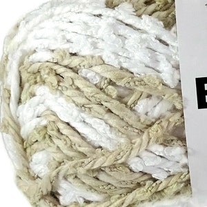 May include: A ball of Bernat Lovie yarn in white and tan colors. The label indicates it is 100% polyester, weighs 3 oz (85 g), and is approximately 77 yards (70 m). The brand name and product name are visible.