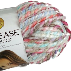 May include: A skein of thick, multi-colored yarn featuring a blend of white, light blue, pink, and brown fibers. The yarn is wrapped in a white paper label that displays the text EASE QUICK and includes a small graphic of a person's face.