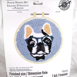 May include: A Loops & Threads punch needle kit featuring a finished 6-inch round embroidery hoop project of a French bulldog wearing glasses. The dog has black, white, and tan fur against a light blue background. The packaging includes text.