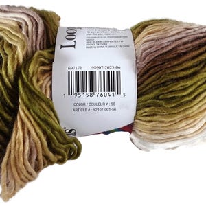 Puede incluir: Una madeja de hilo matizado con un degradado en tonos verde oliva, beige, crema y marr&oacute;n suave. Una etiqueta de papel blanco envuelve el centro, mostrando un c&oacute;digo de barras, el texto Loop y los n&uacute;meros de identificaci&oacute;n 697171 98907-2023-06.
