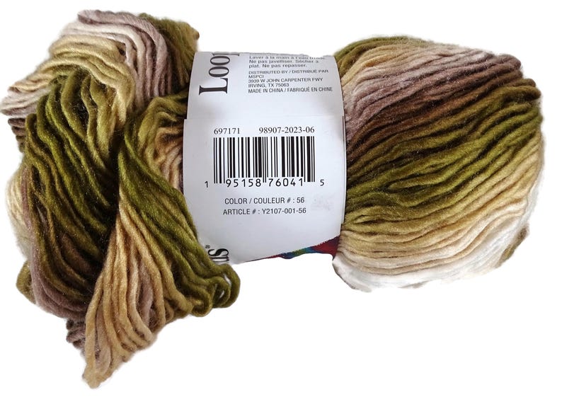 Puede incluir: Una madeja de hilo matizado con un degradado en tonos verde oliva, beige, crema y marr&oacute;n suave. Una etiqueta de papel blanco envuelve el centro, mostrando un c&oacute;digo de barras, el texto Loop y los n&uacute;meros de identificaci&oacute;n 697171 98907-2023-06.