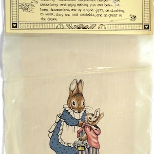 May include: A hand silk-screened fabric panel in a clear plastic bag with a header card. The card reads: hand silk-screened fabric panels. TRULY a special medium when CREATING TREASURED KEEPSAKES. The fabric features a brown rabbit in a blue dress.