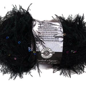 May include: A skein of black eyelash yarn featuring scattered multicolored sequins throughout the fibers. A white paper label wraps around the center, displaying the Loops & Threads brand logo and the product name Eyelash Sequin in black text.