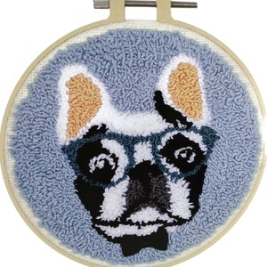 May include: A handmade punch needle embroidery hoop art featuring a dog wearing glasses and a bow tie. The dog's face is black, white, and tan, set against a light blue background. The embroidery is framed in a wooden hoop.