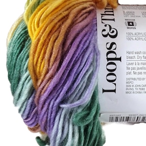 May include: A skein of medium weight 4 acrylic yarn featuring a variegated color palette of green, yellow, orange, and purple. The white paper label displays the brand name Loops & Threads, care instructions, and a barcode on a white background.