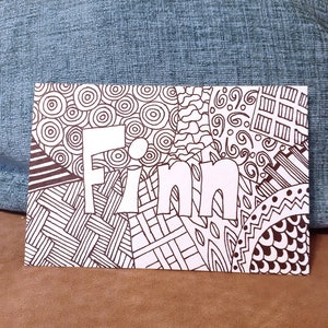 May include: A white card with the name "Finn" written in large, bold, white letters. The card is decorated with black and white abstract patterns.