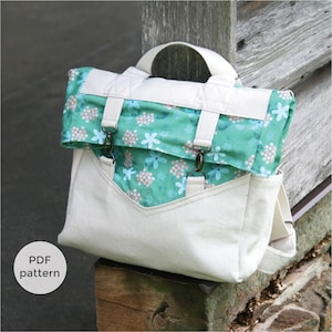 May include: A white canvas backpack with a green and white floral fabric flap. The backpack has two adjustable straps and a handle. The text "PDF pattern" is visible in the lower left corner of the image.
