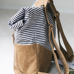 K&ouml;nnte beinhalten: Ein gestreifter schwarz-wei&szlig;er Canvas-Rucksack mit braunen Lederriemen und einem braunen Lederboden.