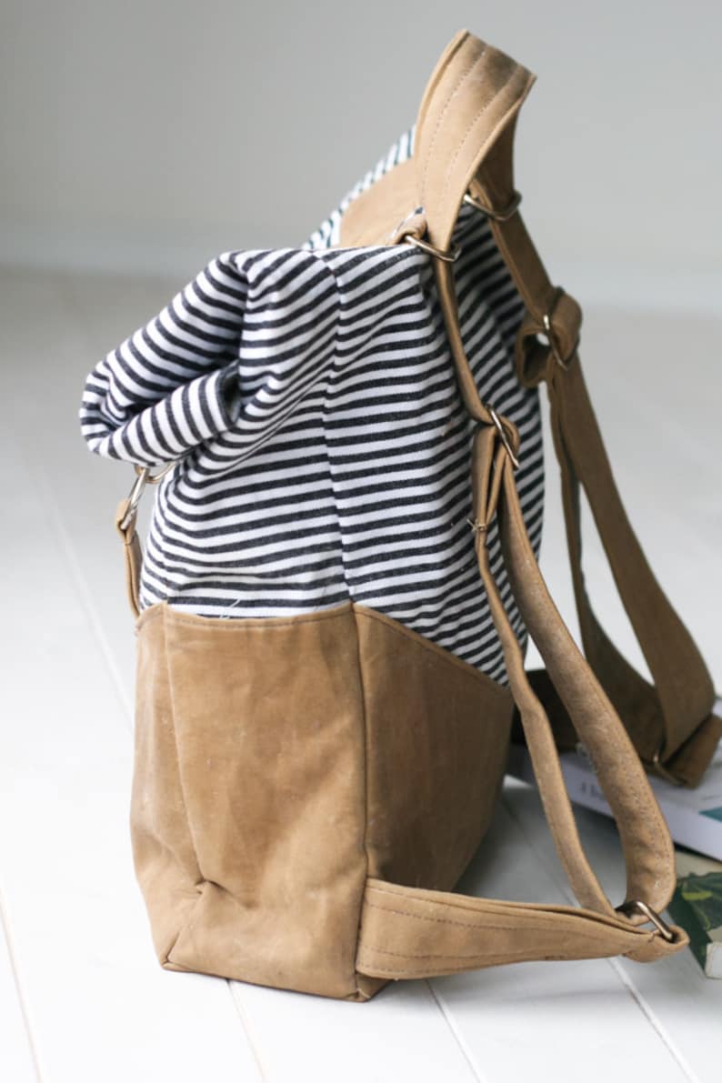 K&ouml;nnte beinhalten: Ein gestreifter schwarz-wei&szlig;er Canvas-Rucksack mit braunen Lederriemen und einem braunen Lederboden.