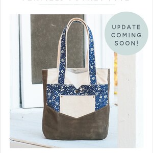 May include: The Penfield Pocket Tote bag features a brown suede-like bottom, a cream-colored pocket, and a blue floral patterned top. The tote has cream-colored handles and the text "UPDATE COMING SOON!" in a circle.