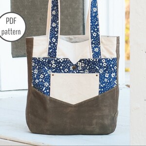 May include: A canvas tote bag with a brown bottom and a cream-colored body. The bag features a blue floral patterned pocket and straps. The text "PDF pattern" is in a white circle in the upper left corner.