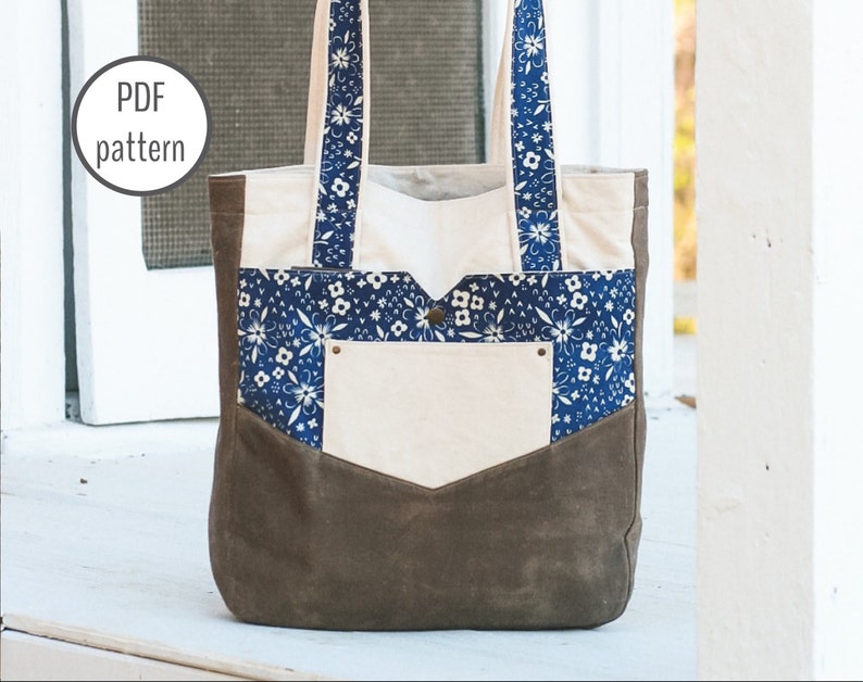 May include: A canvas tote bag with a brown bottom and a cream-colored body. The bag features a blue floral patterned pocket and straps. The text "PDF pattern" is in a white circle in the upper left corner.