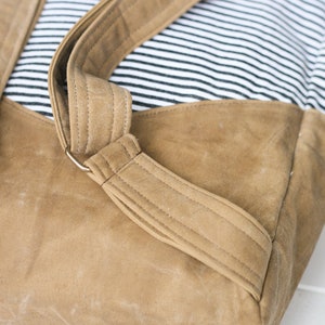 K&ouml;nnte beinhalten: Ein brauner Canvas-Rucksack mit gestreiftem Stofffutter und verstellbaren Tr&auml;gern. Die Tr&auml;ger sind aus braunem Canvas-Material und haben Metallschnallen.
