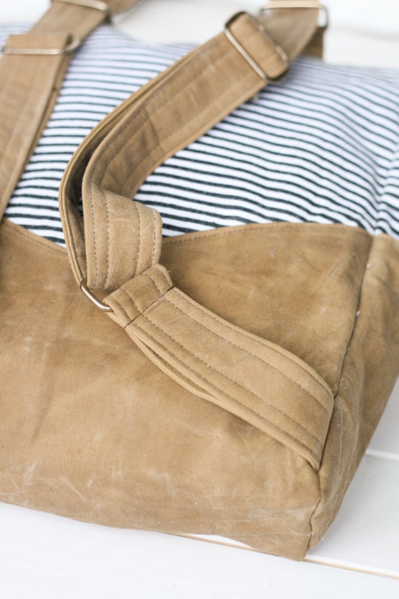 K&ouml;nnte beinhalten: Ein brauner Canvas-Rucksack mit gestreiftem Stofffutter und verstellbaren Tr&auml;gern. Die Tr&auml;ger sind aus braunem Canvas-Material und haben Metallschnallen.