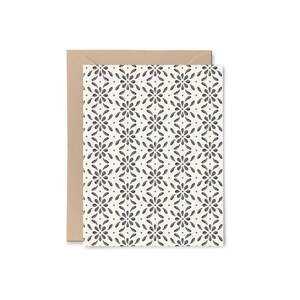 May include: A greeting card with a floral pattern in black and white, accompanied by a brown envelope. The card's design features a repeating pattern of stylized flowers and dots on a cream background.