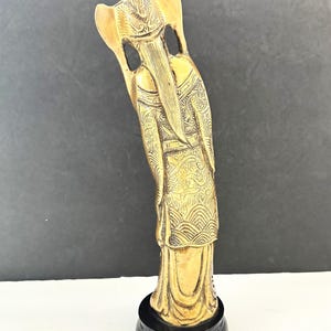 May include: A gold-colored statue of a figure with long hair and ornate clothing, standing on a black base. The statue has detailed patterns and a serene expression, likely representing a deity or historical figure.