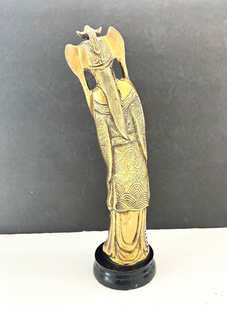 May include: A gold-colored statue of a figure with long hair and ornate clothing, standing on a black base. The statue has detailed patterns and a serene expression, likely representing a deity or historical figure.