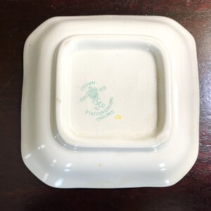 Pode incluir: Um prato quadrado branco com um logotipo verde e branco que diz "Crown Est 1801 Staffordshire England".
