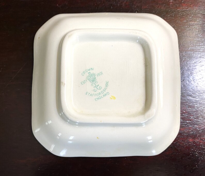 Pode incluir: Um prato quadrado branco com um logotipo verde e branco que diz "Crown Est 1801 Staffordshire England".