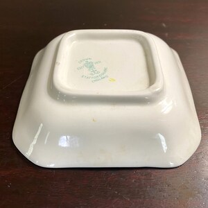 Pode incluir: Um prato quadrado branco com um logotipo verde e branco que diz "Crown, Est'd 1801, Staffordshire, England".