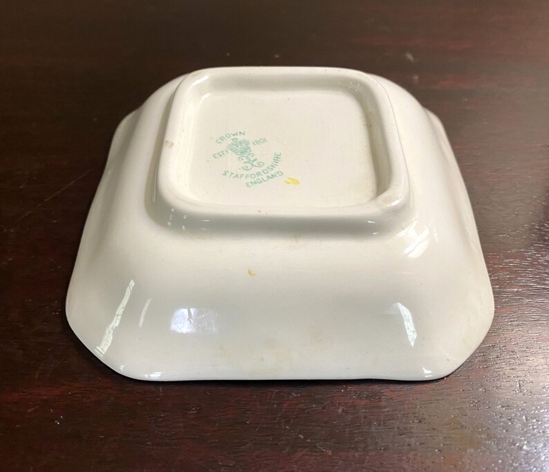 Pode incluir: Um prato quadrado branco com um logotipo verde e branco que diz "Crown, Est'd 1801, Staffordshire, England".