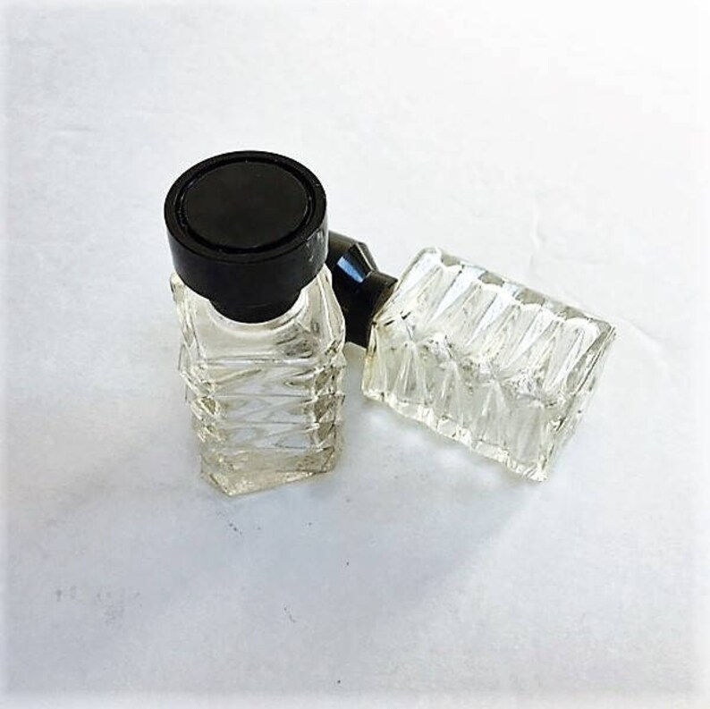 May include: Two clear glass perfume bottles with black plastic tops. The bottles have a textured design.