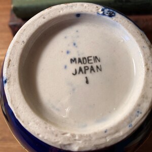 May include: Bottom view of a ceramic vase with a white interior and a blue exterior. The words "MADE IN JAPAN" are printed in black ink on the white base. A small number "1" is printed below the text.