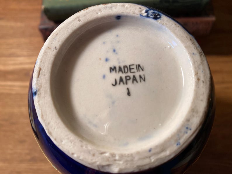 May include: Bottom view of a ceramic vase with a white interior and a blue exterior. The words "MADE IN JAPAN" are printed in black ink on the white base. A small number "1" is printed below the text.