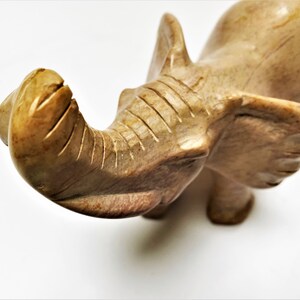 May include: A hand-carved stone elephant figurine with a light brown color. The elephant's trunk is raised and curled, and its ears are spread out.
