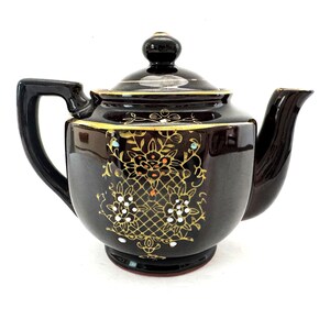 May include: A brown teapot with gold and white floral designs and accents. The teapot has a lid and a spout.