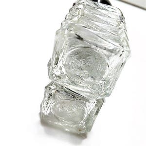 May include: A clear glass bottle with a textured surface. The bottle is stacked on top of another clear glass bottle with a textured surface.
