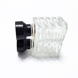 May include: A clear glass bottle with a textured surface and two black plastic stoppers. The bottle is designed to hold liquids.