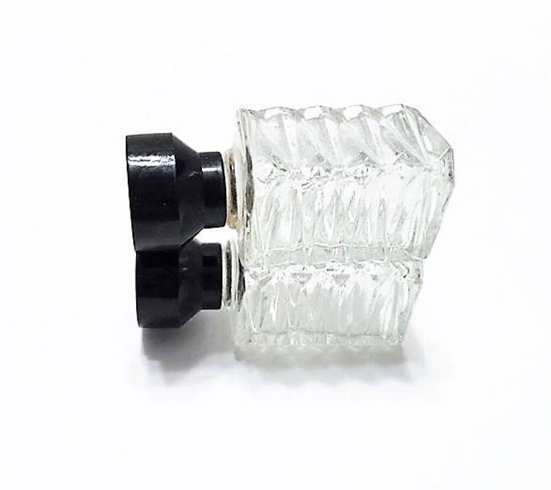 May include: A clear glass bottle with a textured surface and two black plastic stoppers. The bottle is designed to hold liquids.