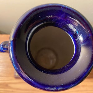 May include: A cobalt blue ceramic vase with a wide opening and two decorative handles. The vase has a glossy finish and a light interior. The top-down perspective highlights the vase's shape and color.