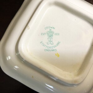 Pode incluir: Close-up da parte inferior de um prato de cer&acirc;mica branca com um logotipo verde e branco que diz "Crown Est 1801 Staffordshire England".