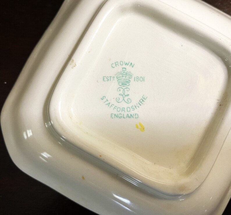 Pode incluir: Close-up da parte inferior de um prato de cer&acirc;mica branca com um logotipo verde e branco que diz "Crown Est 1801 Staffordshire England".