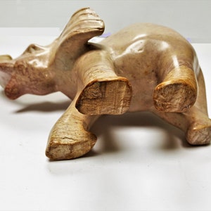 May include: A carved stone elephant figurine with a light brown and beige color. The elephant is standing on all four legs with its trunk raised.