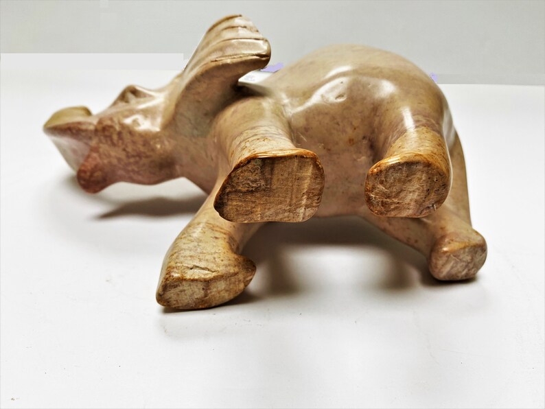 May include: A carved stone elephant figurine with a light brown and beige color. The elephant is standing on all four legs with its trunk raised.