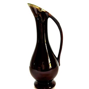 May include: A dark brown ceramic pitcher with a wide, rounded base and a slender neck. The pitcher has a single handle and a glossy finish.