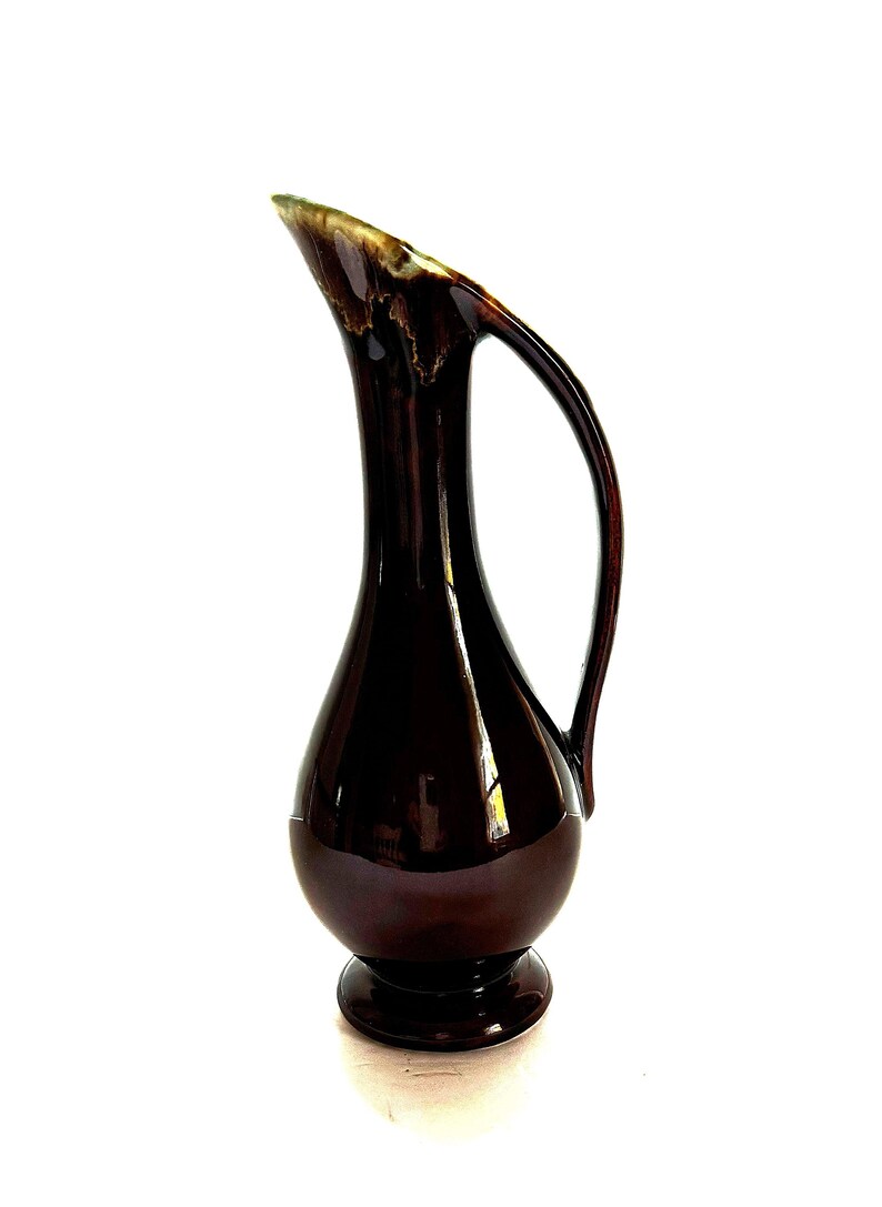 May include: A dark brown ceramic pitcher with a wide, rounded base and a slender neck. The pitcher has a single handle and a glossy finish.