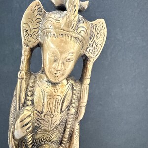 May include: A detailed bronze-colored figurine of a person with ornate headdress and clothing. The figure has a serene expression and holds objects on either side of the head. The statue is approximately 6 inches tall.