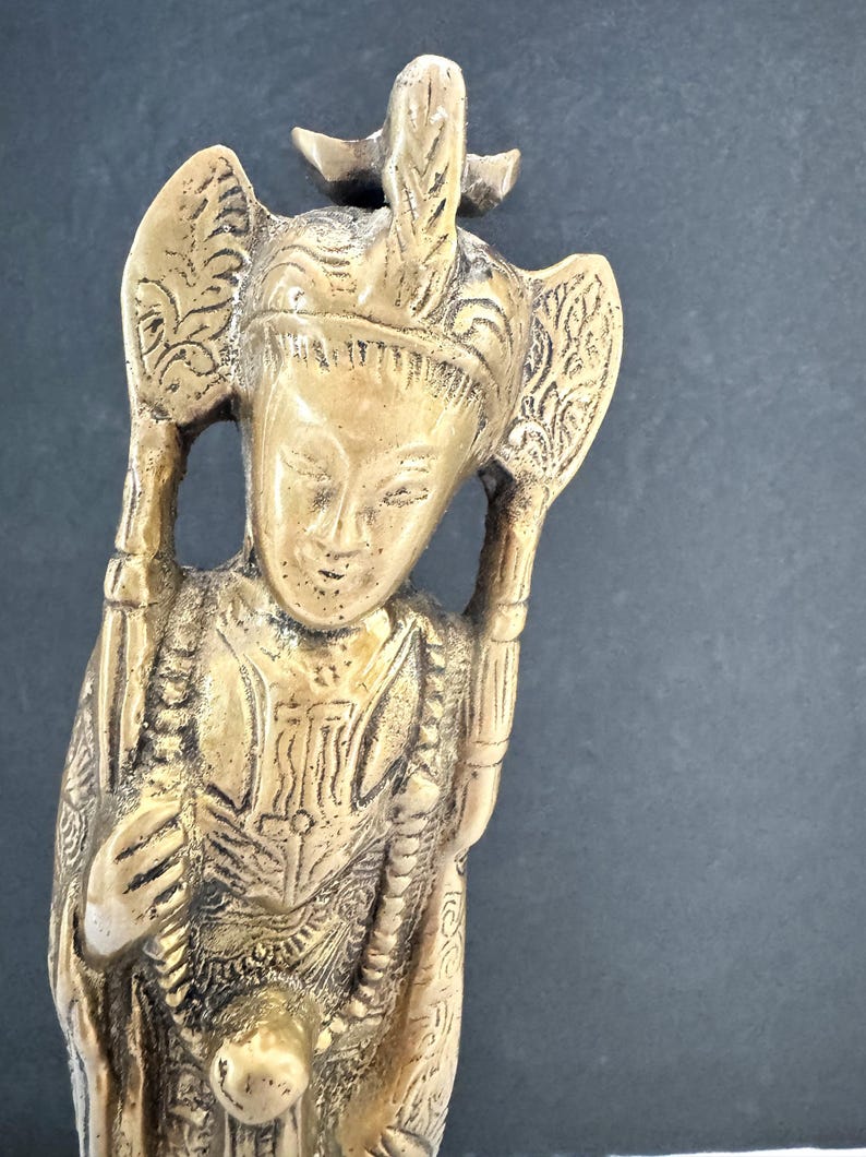 May include: A detailed bronze-colored figurine of a person with ornate headdress and clothing. The figure has a serene expression and holds objects on either side of the head. The statue is approximately 6 inches tall.