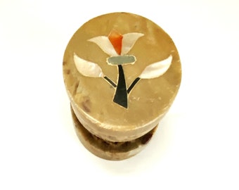 May include: A small, round, beige stone box with a floral design. The design is made of inlaid pieces of different colored stones, including white, orange, and black.