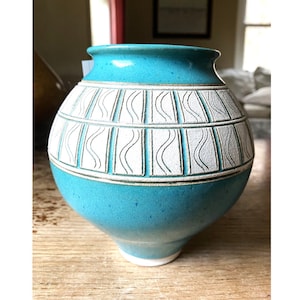 May include: A turquoise ceramic vase with a white geometric pattern. The vase has a rounded body and a small, round base.