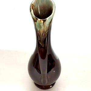 May include: A brown ceramic vase with a flared opening and a green and brown glaze. The vase has a unique shape with a curved neck and a rounded base.