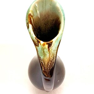 May include: A brown and green ceramic vase with a unique, curved spout. The vase has a mottled glaze with brown, green, and white accents.